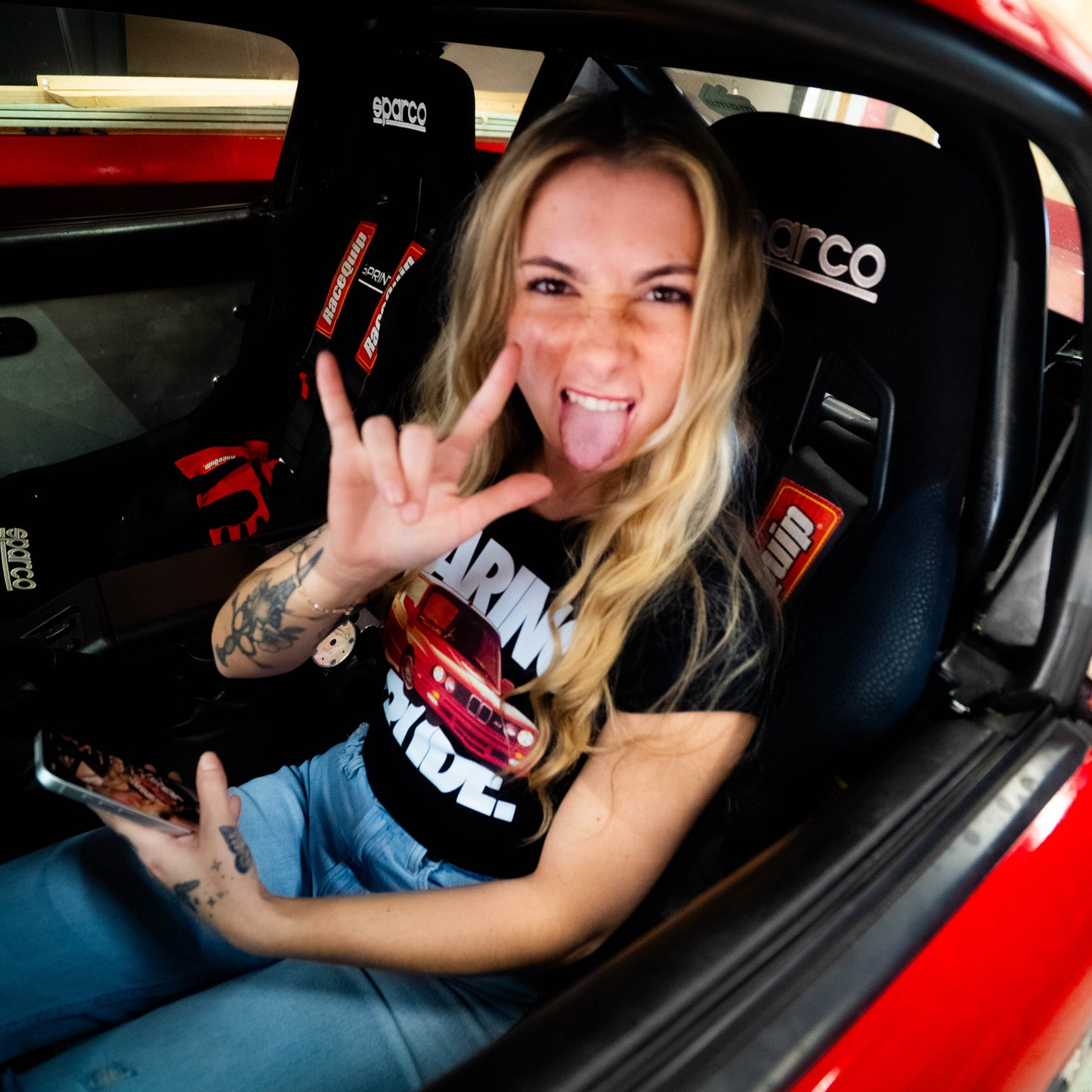 Person sitting in a red car, making a i love you sign