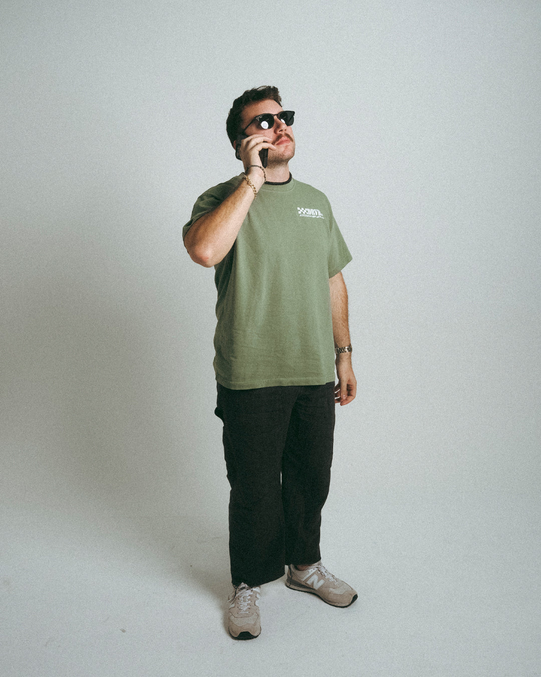 Man wearing green oversized Porsche Widowmaker shirt while holding phone