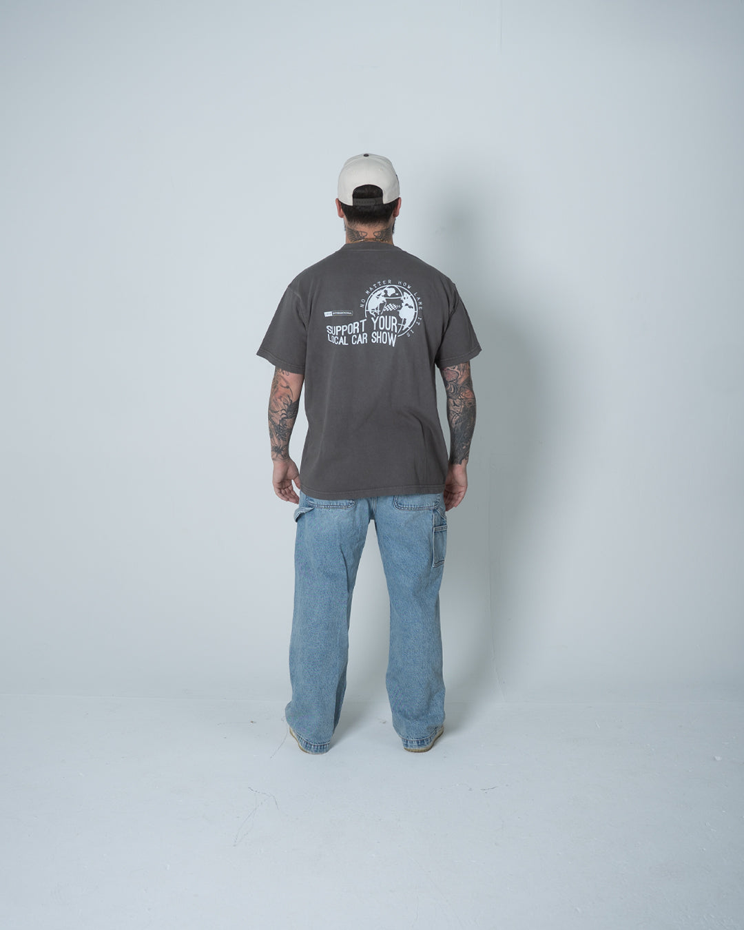 Person wearing a gray t-shirt with a logo and text, standing against a white background