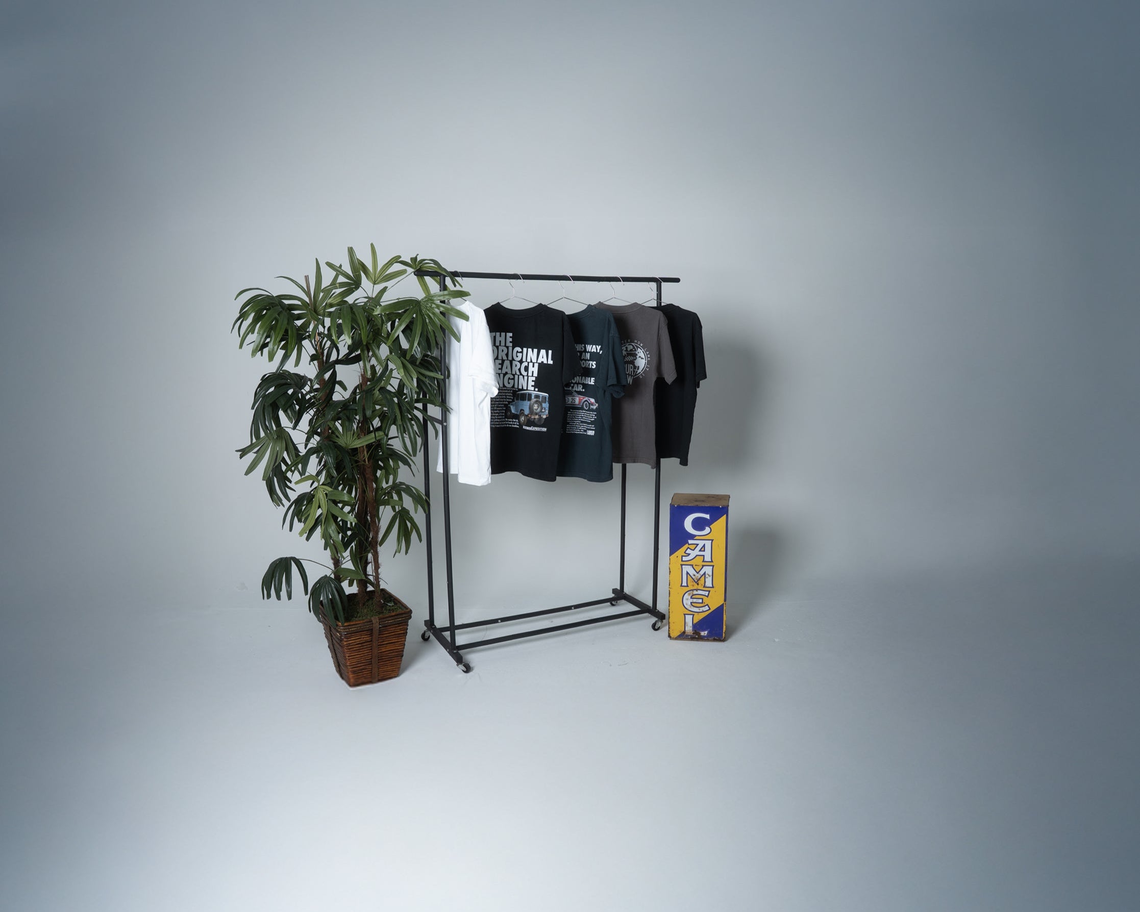 T-shirt rack with t-shirts and a plant on a gray background