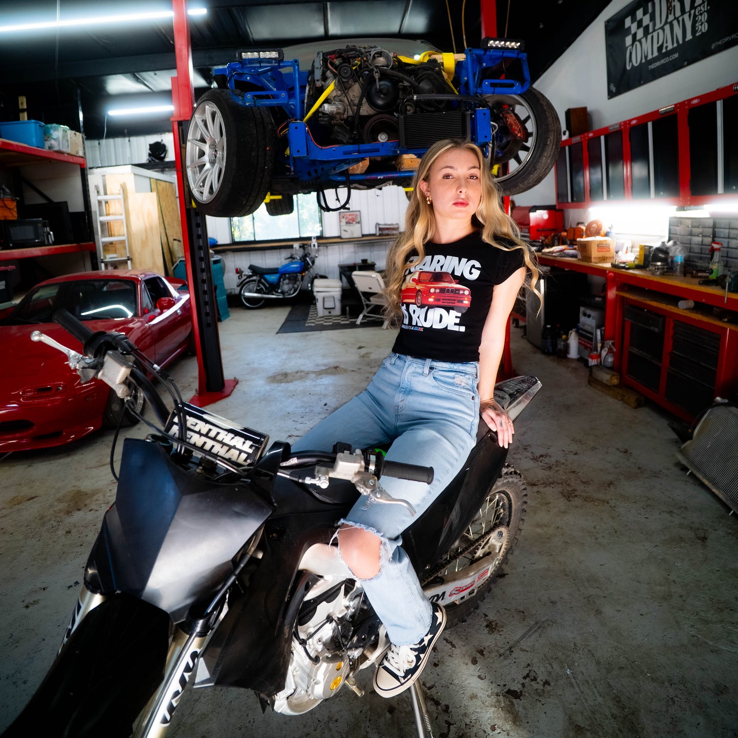 Woman sitting on a motorcycle in a garage with a car on a lift in the background