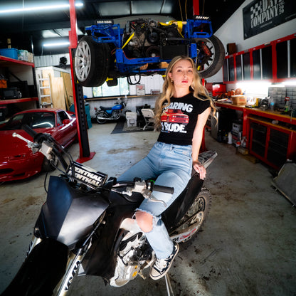 Woman sitting on a motorcycle in a garage with a car on a lift in the background