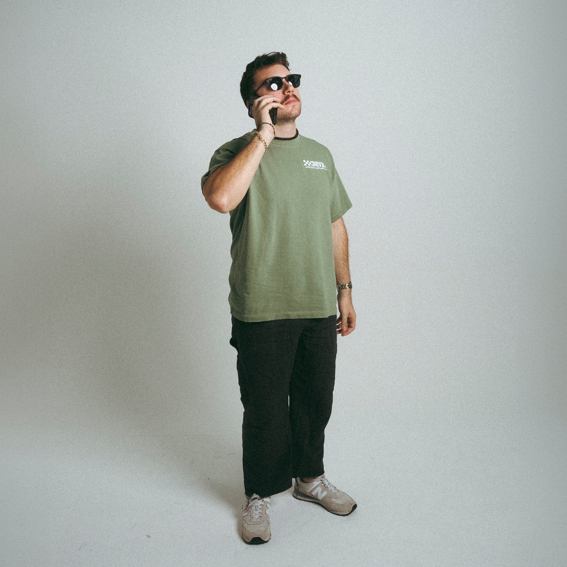 Man holding phone in sunglasses wearing DRVR CO green heavyweight shirt