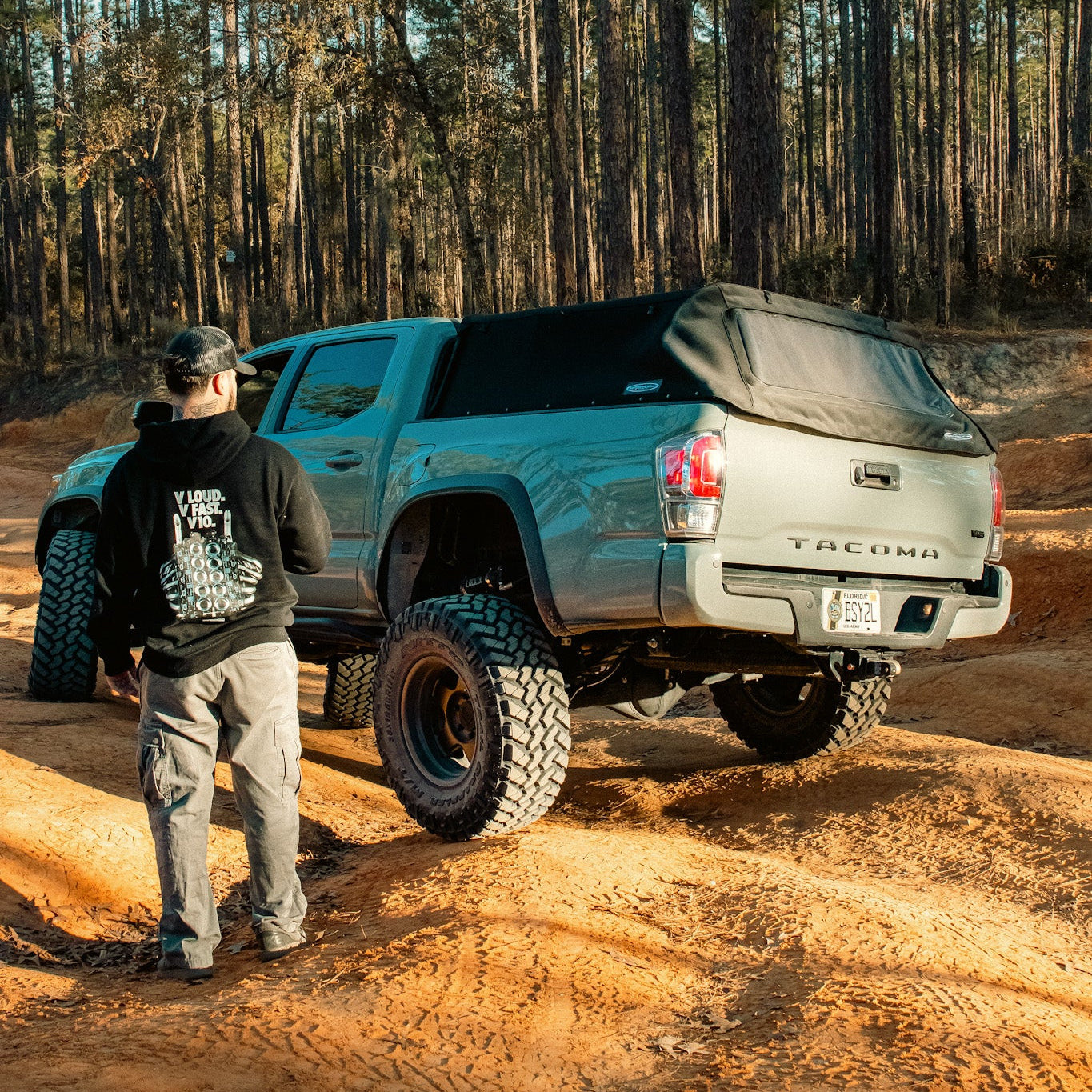 Person standing next to a silver Toyota Tacoma truck in a forested area