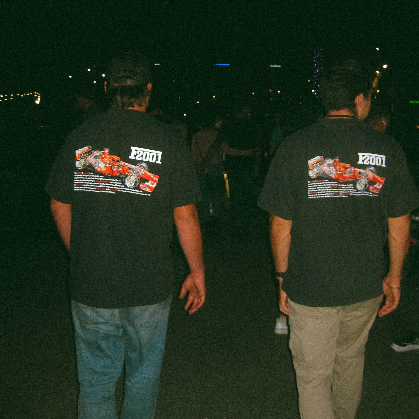 Two people wearing black t-shirts with a racing car design on the back, walking at night.