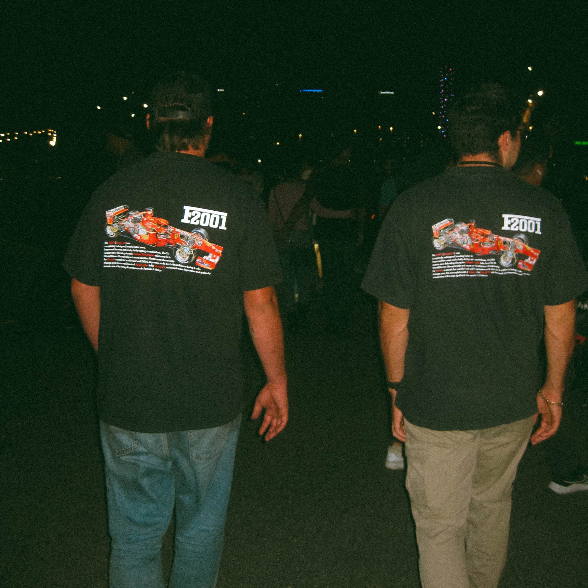 Two people wearing black t-shirts with a racing car design on the back, walking at night.