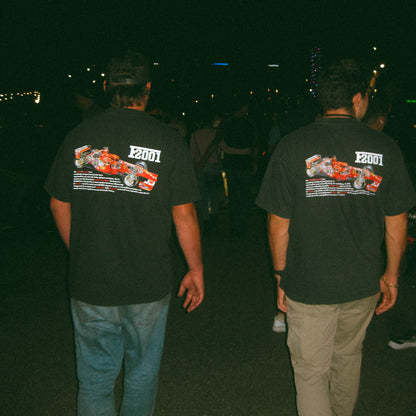 Two people wearing black t-shirts with a racing car design on the back, walking at night.