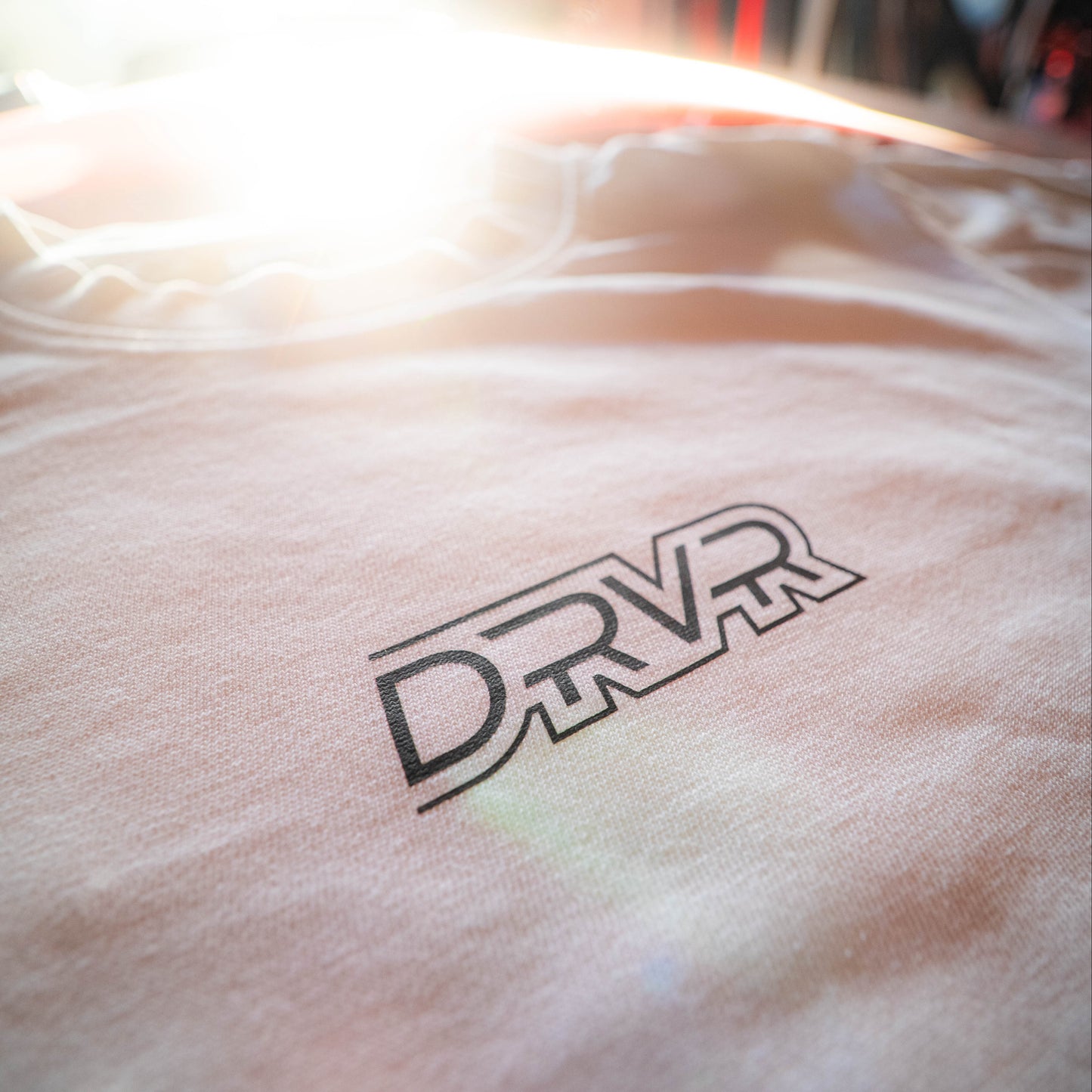 Close-up of a white shirt with 'DRVR' logo on a blurred background