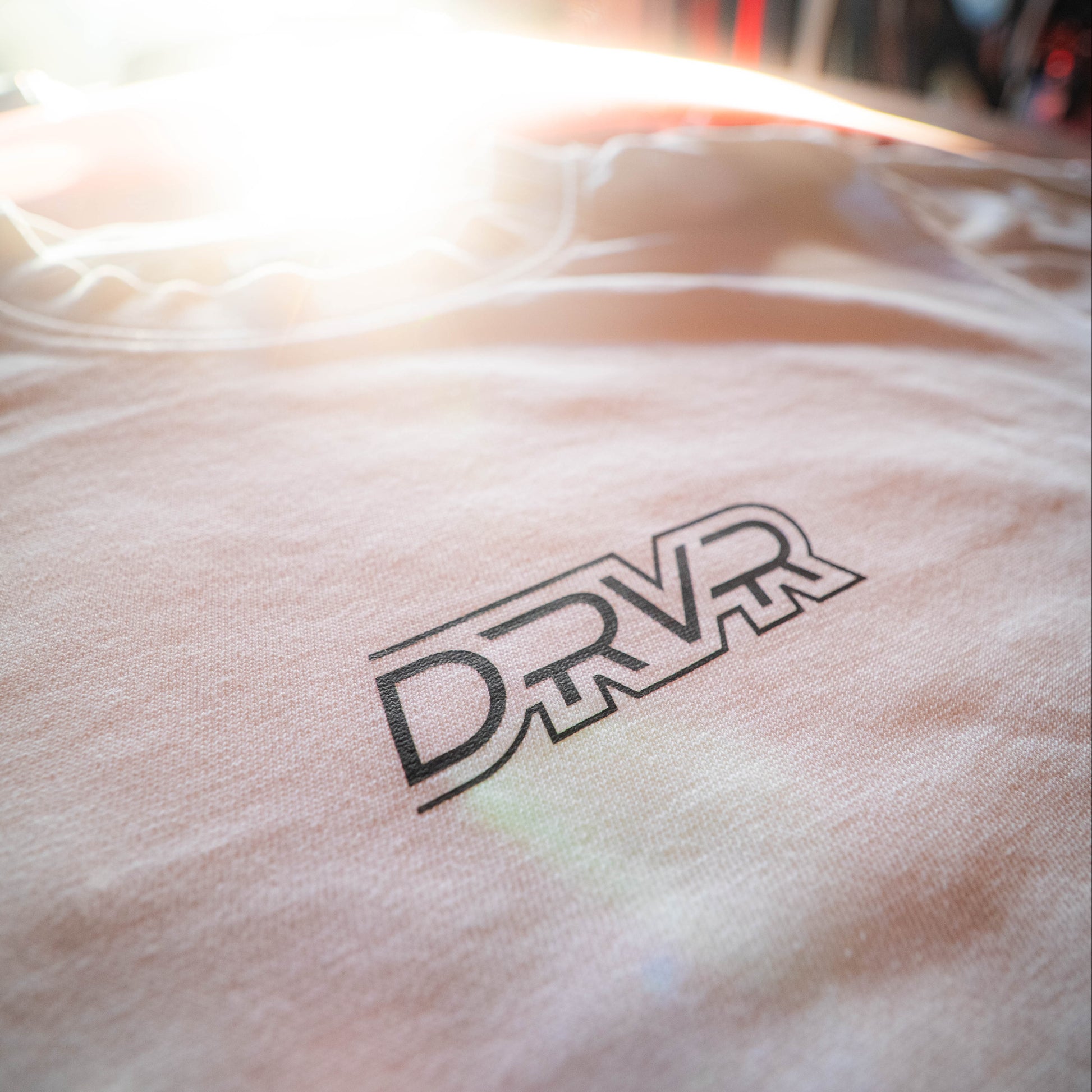 Close-up of a white shirt with 'DRVR' logo on a blurred background