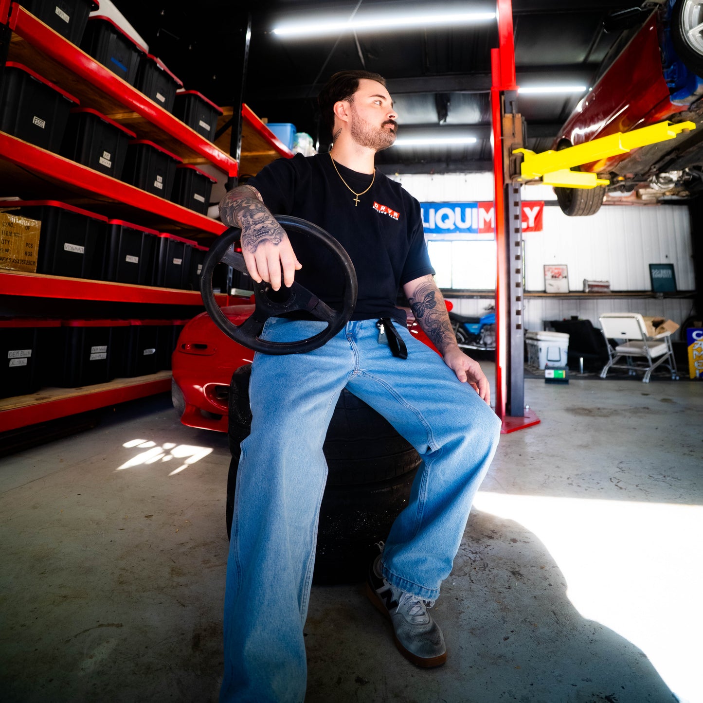 Man sitting on a car seat in a garage with shelves and equipment in the background