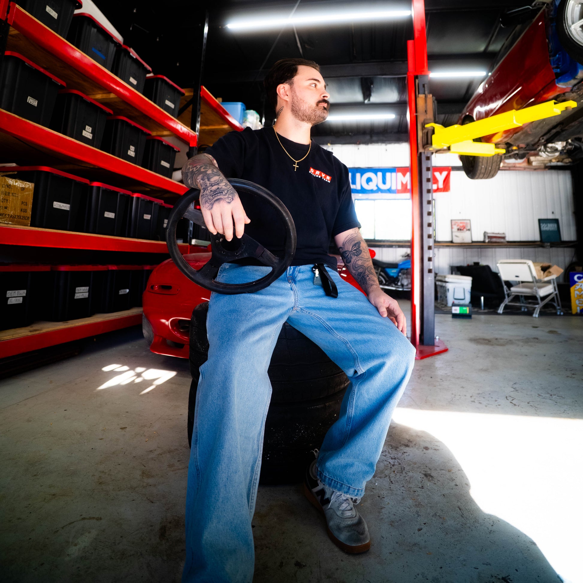 Man sitting on a car seat in a garage with shelves and equipment in the background