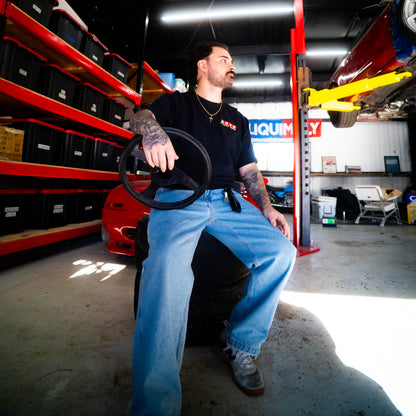 Man sitting on a car seat in a garage with shelves and equipment in the background