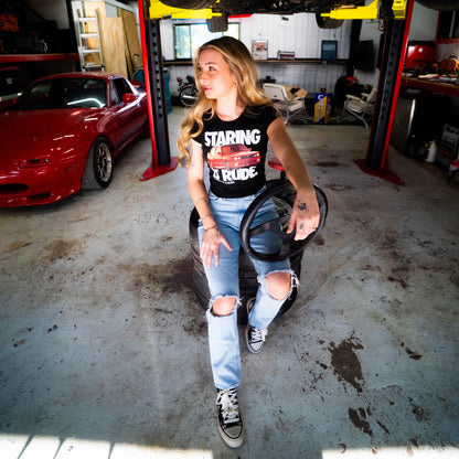 Person sitting on a car tire in a garage with a red car and tools in the background