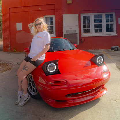 Person leaning against a red car in front of a red building with blue sky.