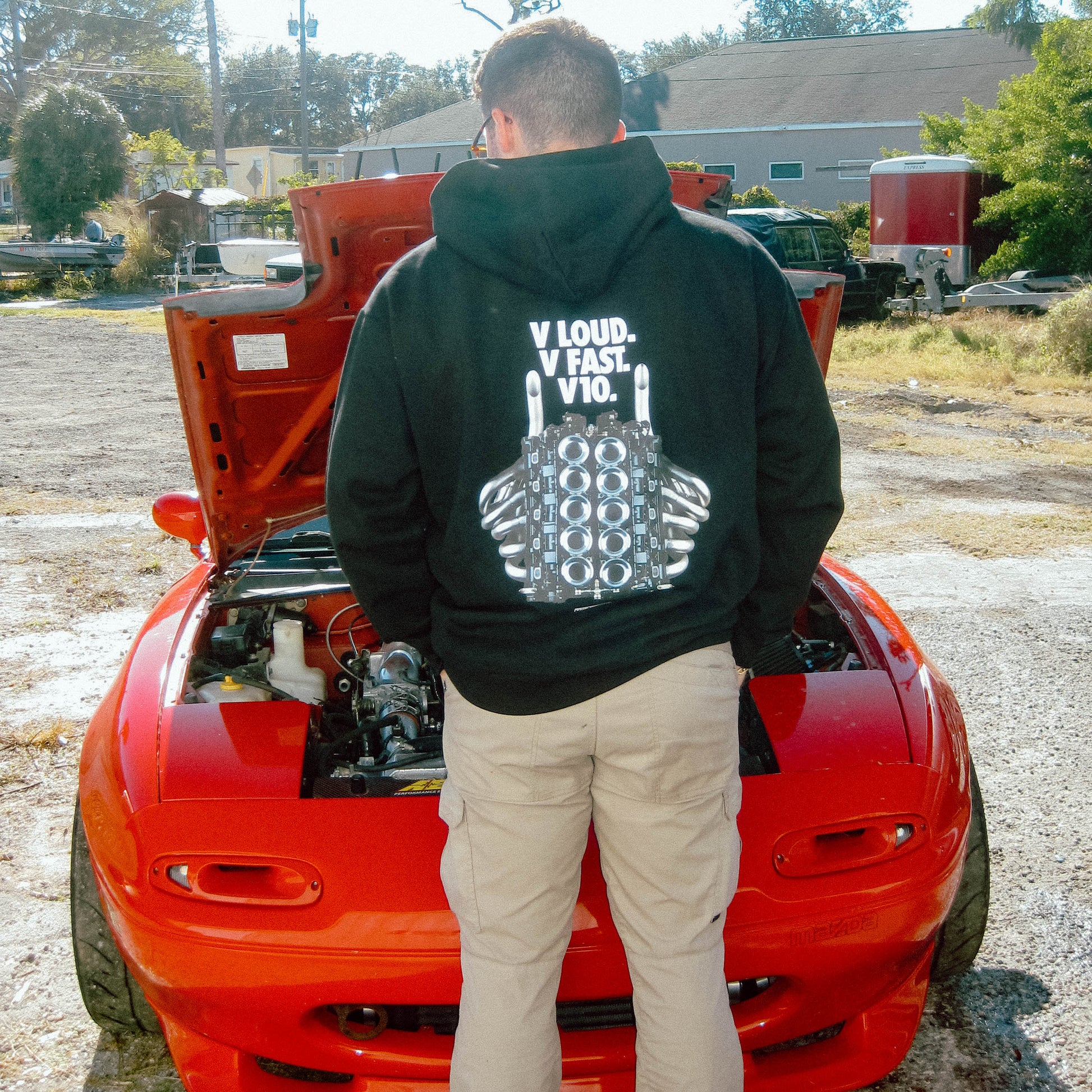 Man standing in black hoodie in front of red car