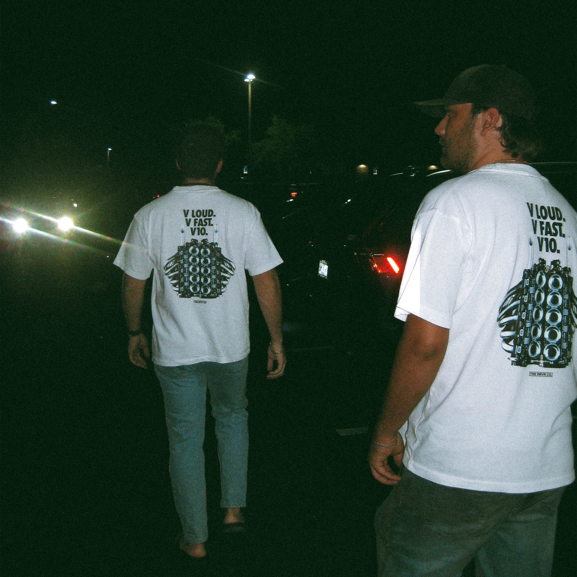 Two people wearing white t-shirts with graphics and text walking at night.