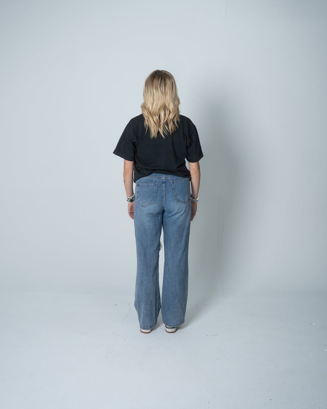 Person wearing a black t-shirt and blue jeans standing against a plain white background