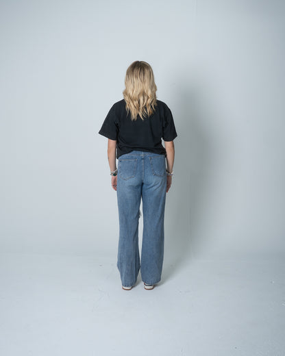 Person wearing a black t-shirt and blue jeans standing against a plain white background