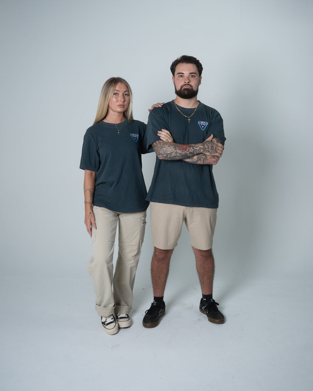 Two people wearing matching dark shirts and light pants on a plain background