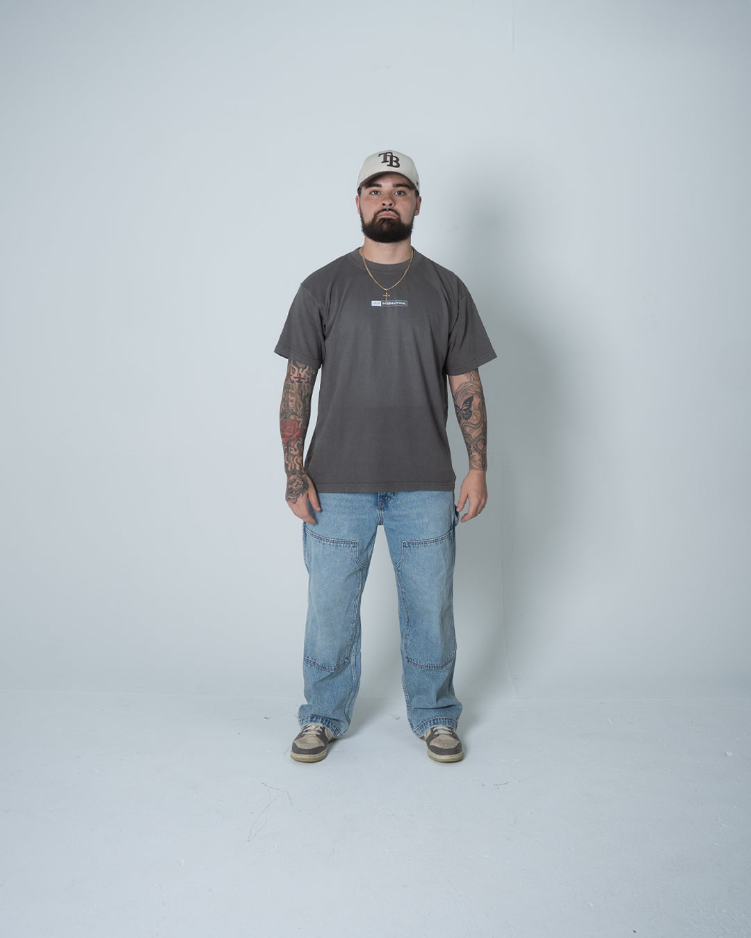Man wearing a gray t-shirt and blue jeans standing against a white background