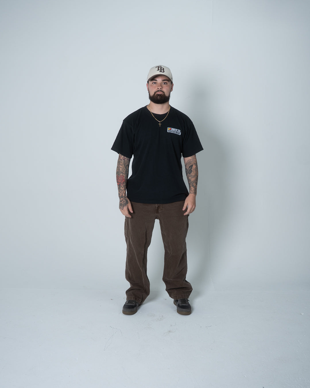 Man wearing a black t-shirt, brown pants, and a cap on a white background