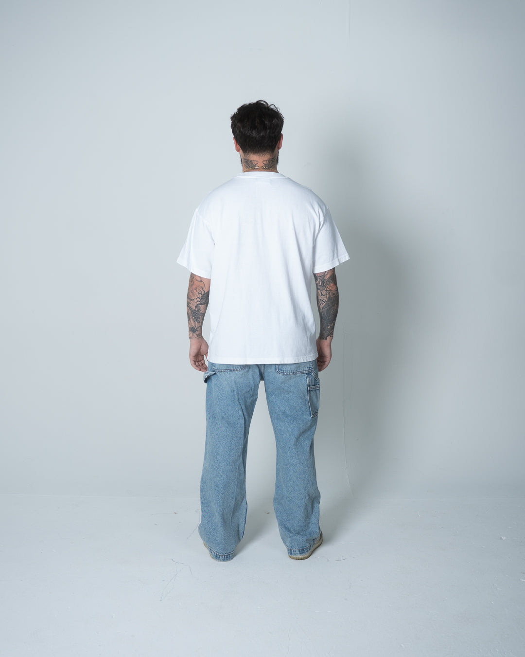 Person wearing a white t-shirt and light blue jeans on a plain background