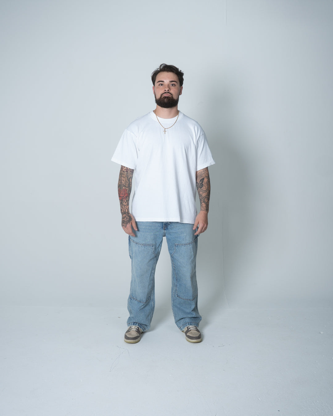 Man wearing a white t-shirt and blue jeans standing against a plain background