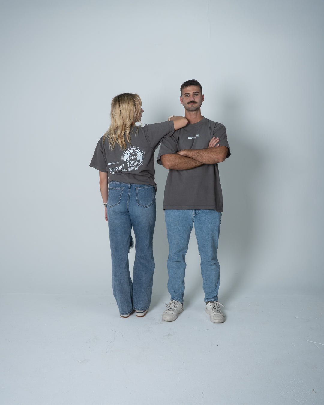 Two people wearing matching gray t-shirts and blue jeans standing against a plain background