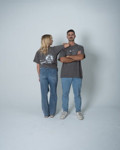Two people wearing matching gray t-shirts and blue jeans standing against a plain background
