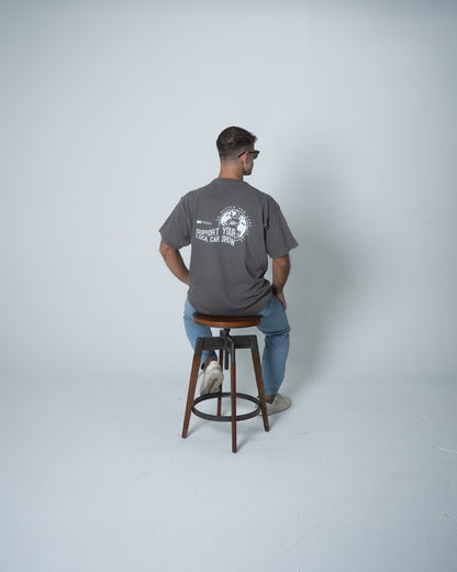 Man sitting on a stool wearing a gray t-shirt with a logo and text on the back.