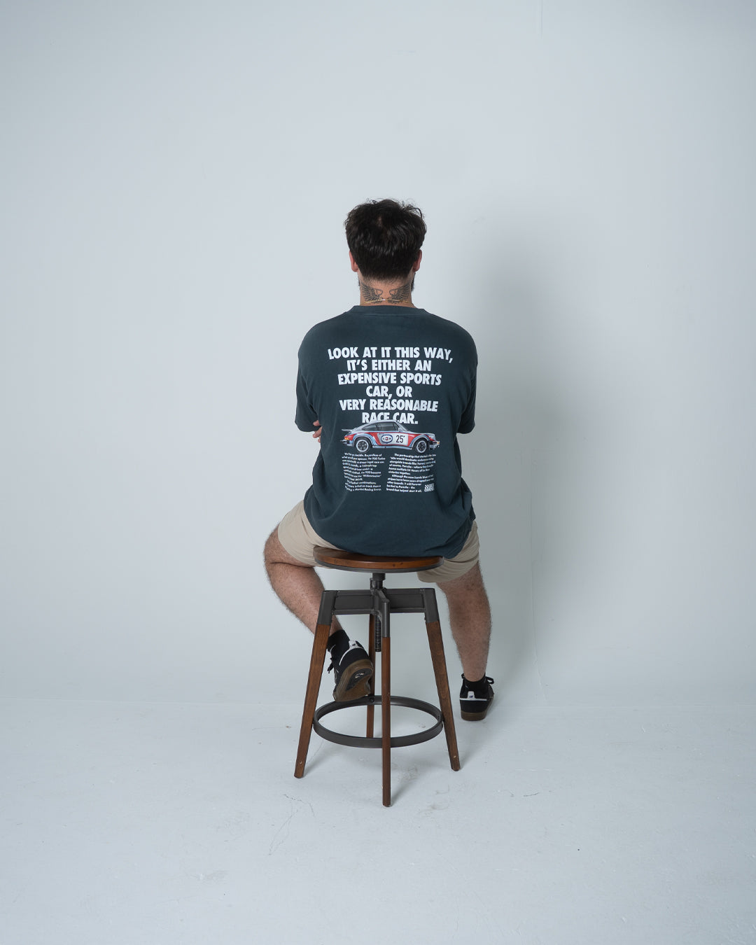 Person wearing a dark blue t-shirt with text and graphics, sitting on a stool against a white background