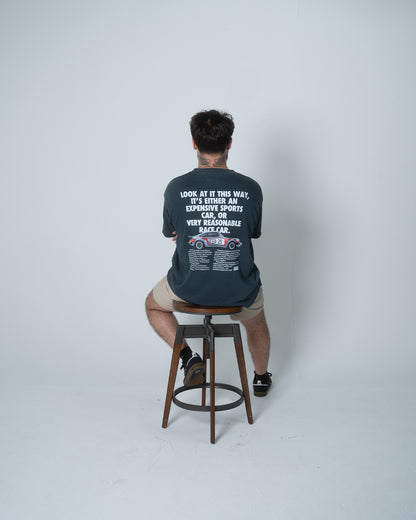Person wearing a dark blue t-shirt with text and graphics, sitting on a stool against a white background