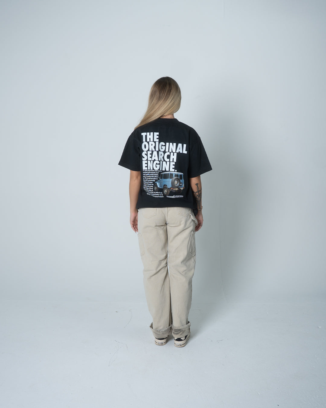 Person wearing a black t-shirt with text on the back, standing against a white background