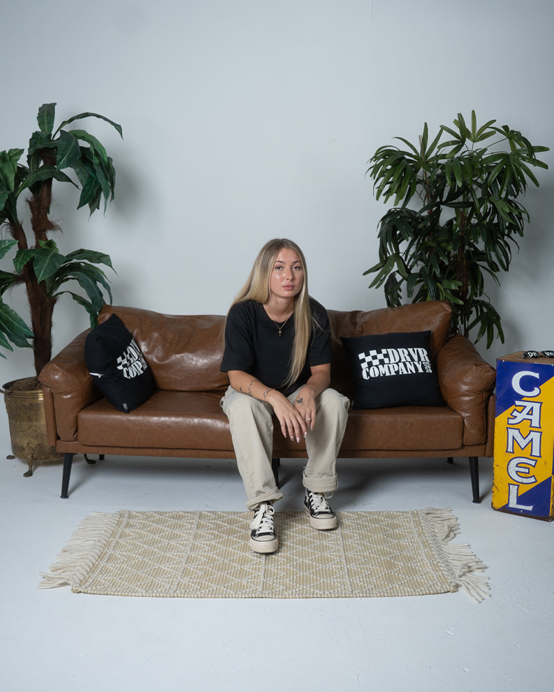 Person sitting on a brown leather couch with plants and a Camel sign in the background